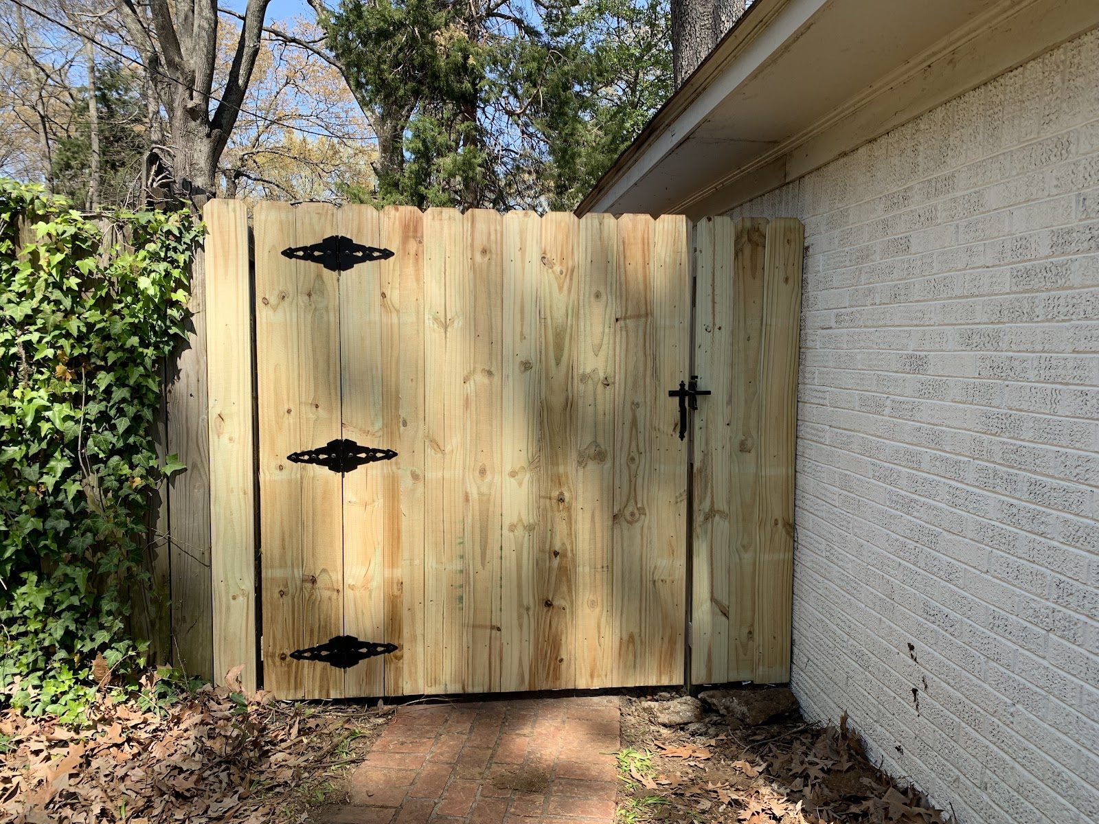 Wood side gate with black hardware beside a brick house